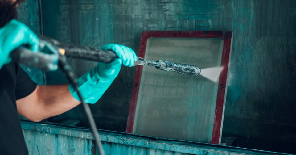 Man cleaning a screen with a hose 